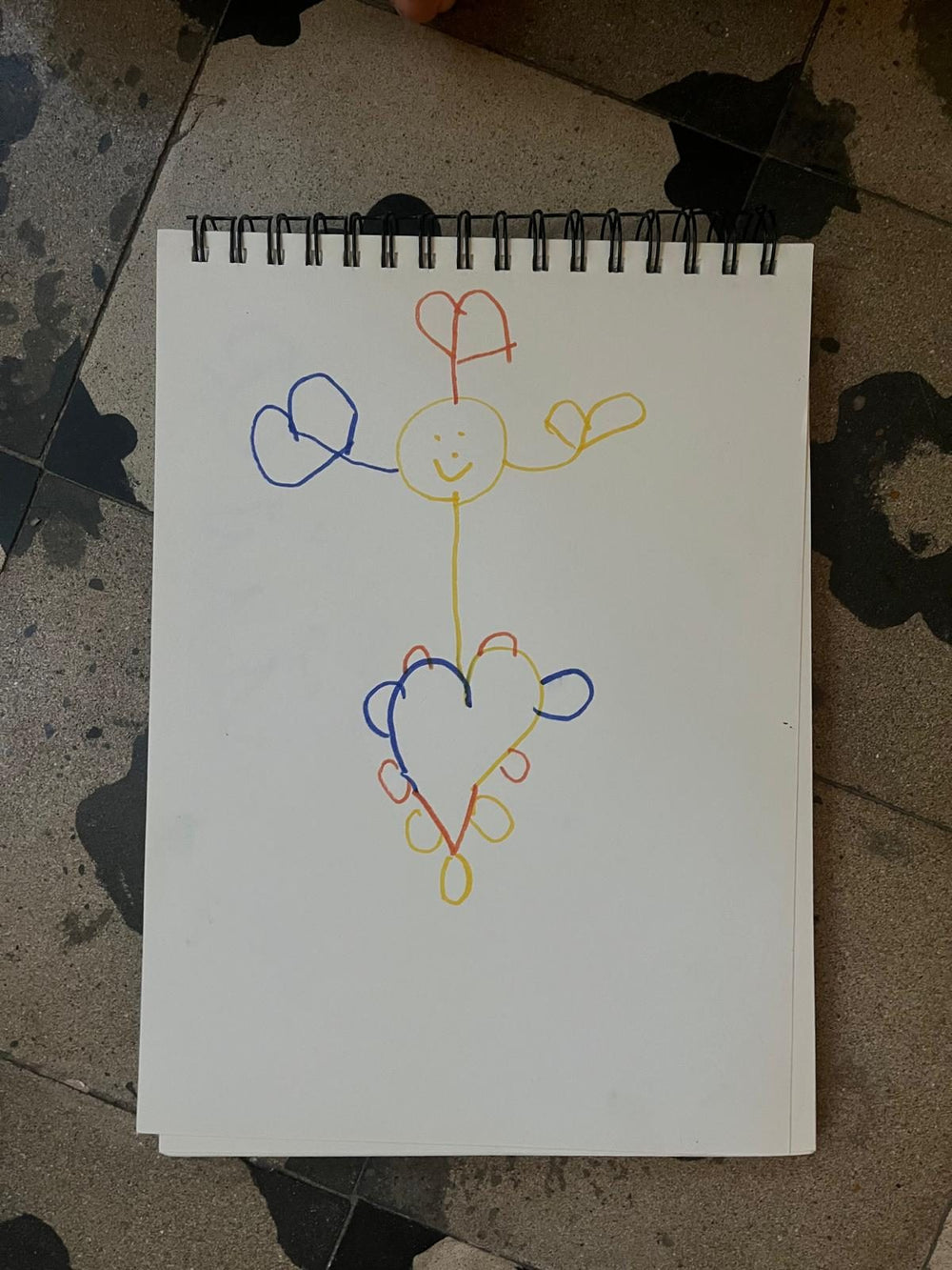 A child’s drawing of a character made of hearts, photographed flat on a sketchbook